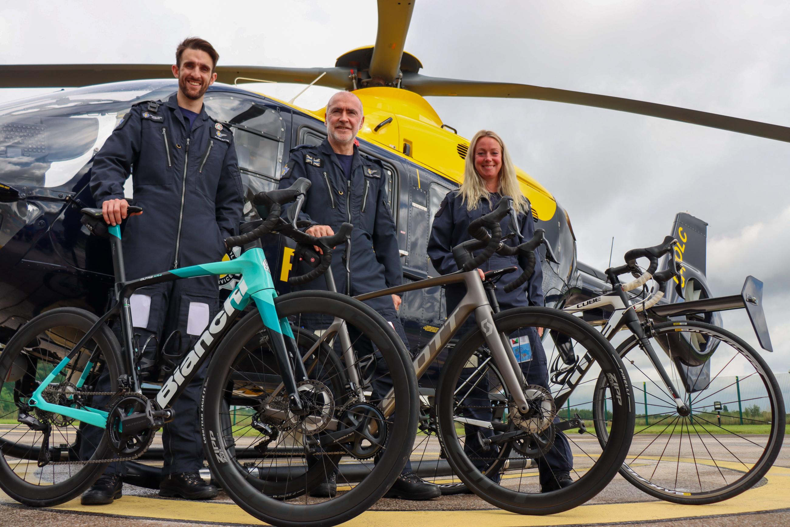 Three Tactical Flight Officers holding their bikes in front of police helicopter