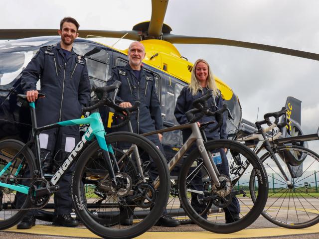 Three Tactical Flight Officers holding their bikes in front of police helicopter